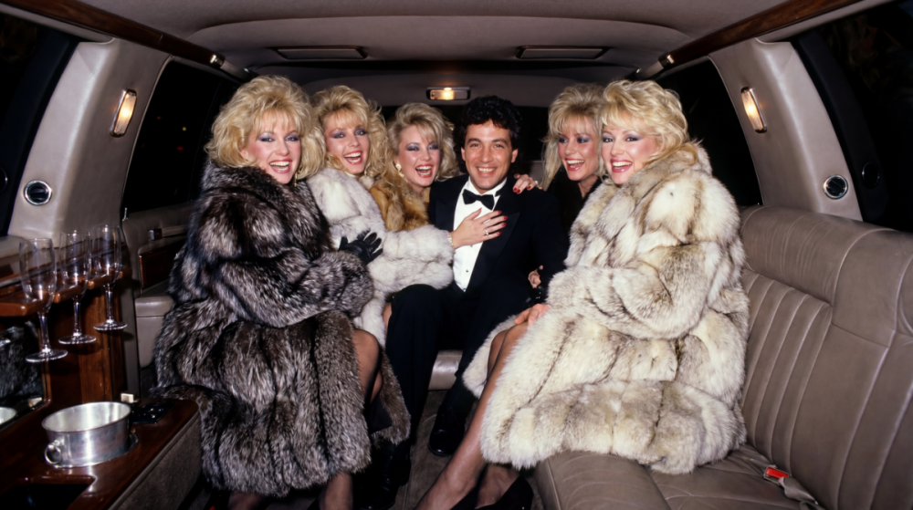 5_glamorous_busty_blonde_80s_models_in_the_back_of_a_limo_wearing_thick_fox_fur_coats_smiling_and_laughing_hugging_a_brunette_man_in_a_tuxedo.thumb.png.1839c376b2ac0e8dbdc500a4c871d2d5.png